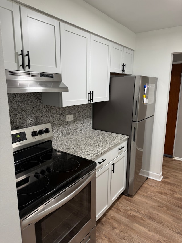 kitchen with light hardwood / wood-style flooring, stainless steel appliances, light stone countertops, white cabinets, and decorative backsplash