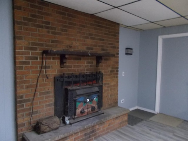 unfurnished living room with a paneled ceiling, wood-type flooring, and a brick fireplace