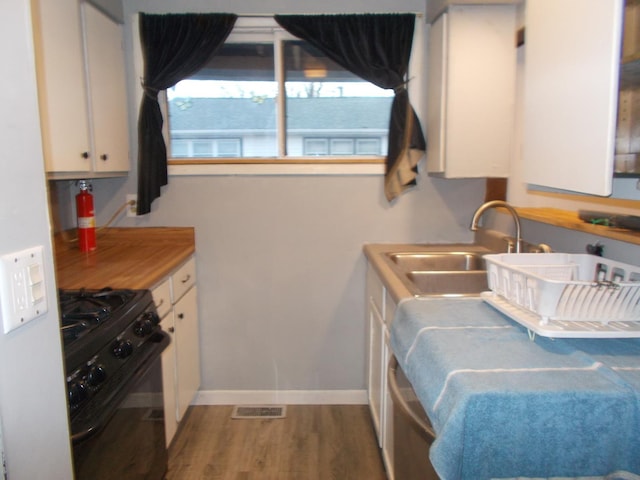 kitchen with black gas range oven, sink, wood-type flooring, and white cabinets