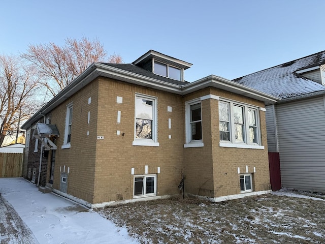 snow covered property featuring fence and brick siding