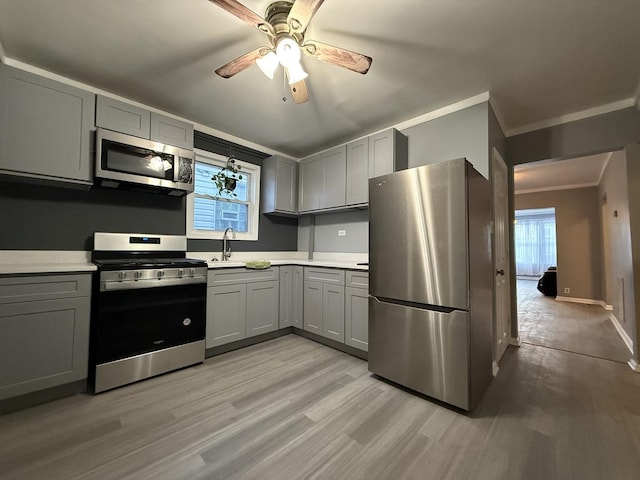 kitchen featuring stainless steel appliances, ornamental molding, gray cabinets, and light hardwood / wood-style flooring