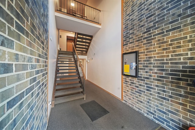 stairs with carpet flooring, brick wall, and a high ceiling