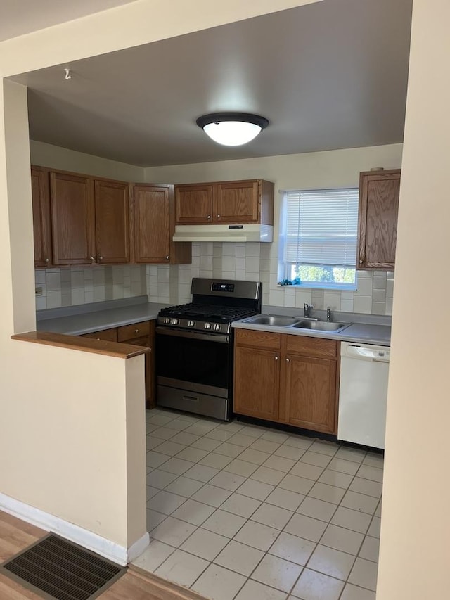 kitchen featuring light tile patterned flooring, sink, gas range, white dishwasher, and decorative backsplash