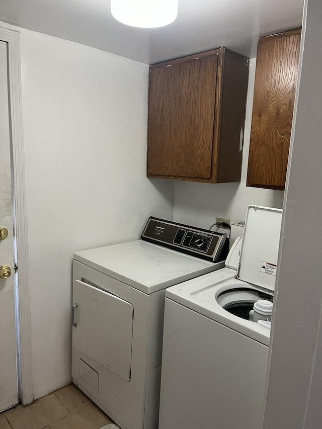 clothes washing area with cabinets, washer and dryer, and light tile patterned floors