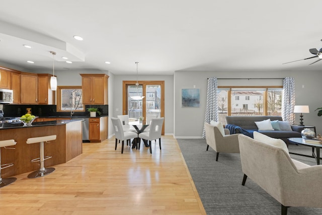 kitchen featuring dark countertops, open floor plan, stainless steel microwave, and light wood finished floors