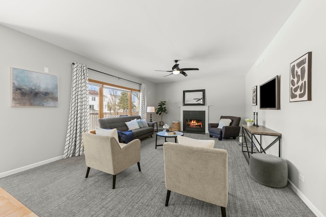 living area with ceiling fan, a tiled fireplace, and baseboards