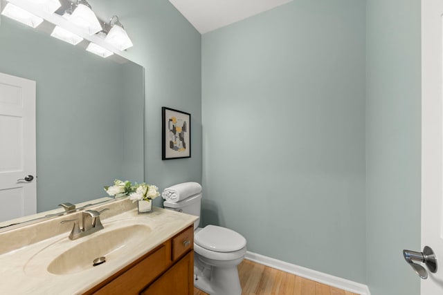 half bath with baseboards, vanity, toilet, and wood finished floors