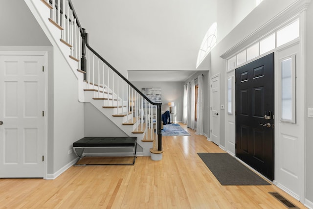 foyer featuring wood finished floors, a towering ceiling, visible vents, baseboards, and stairway