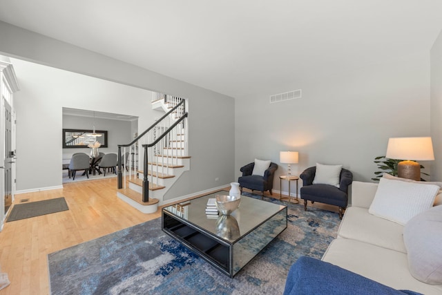 living room with baseboards, stairs, visible vents, and wood finished floors