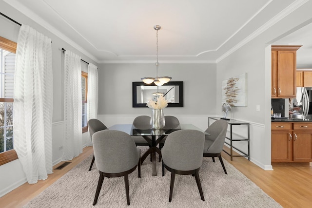 dining room with light wood finished floors, visible vents, and crown molding