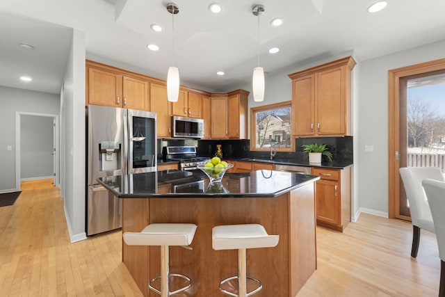 kitchen with appliances with stainless steel finishes, a healthy amount of sunlight, a kitchen island, and light wood-style flooring