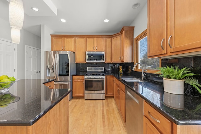 kitchen with light wood finished floors, stainless steel appliances, backsplash, brown cabinetry, and a sink