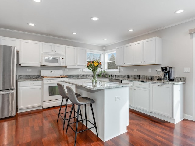 kitchen featuring a kitchen island, light stone counters, white cabinets, and white appliances