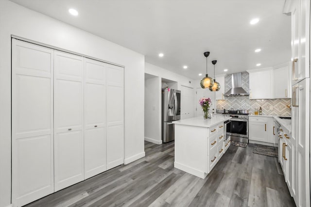 kitchen featuring a kitchen island, appliances with stainless steel finishes, pendant lighting, white cabinetry, and wall chimney range hood