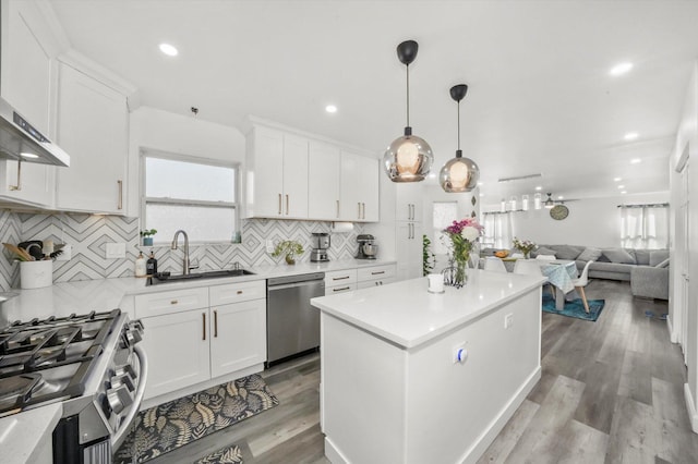 kitchen with sink, white cabinetry, a center island, hanging light fixtures, and stainless steel appliances