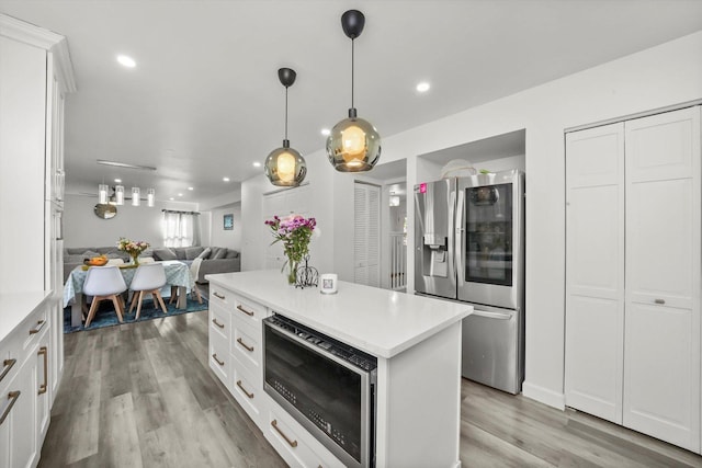 kitchen with stainless steel appliances, white cabinetry, pendant lighting, and light hardwood / wood-style flooring