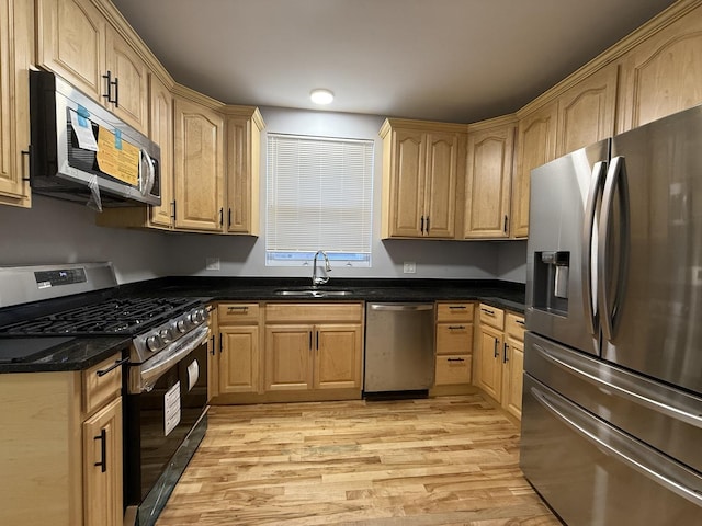 kitchen with appliances with stainless steel finishes, light brown cabinetry, sink, dark stone countertops, and light hardwood / wood-style floors