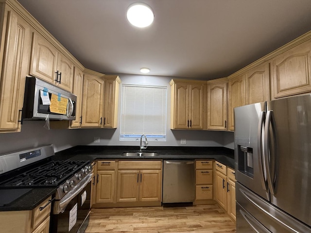 kitchen with light brown cabinetry, sink, dark stone counters, stainless steel appliances, and light hardwood / wood-style flooring