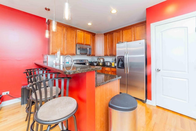 kitchen with a breakfast bar area, decorative light fixtures, appliances with stainless steel finishes, kitchen peninsula, and light hardwood / wood-style floors