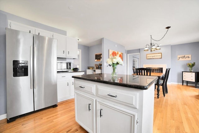 kitchen with hanging light fixtures, light wood-type flooring, appliances with stainless steel finishes, a kitchen island, and white cabinets