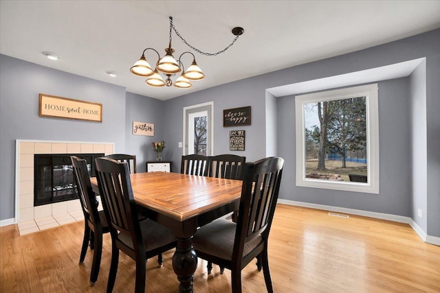 dining room with a tiled fireplace, a chandelier, a wealth of natural light, and light wood-type flooring