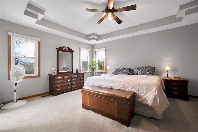 carpeted bedroom with multiple windows, a tray ceiling, and ceiling fan