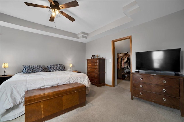 bedroom with ceiling fan, a tray ceiling, a walk in closet, light colored carpet, and a closet