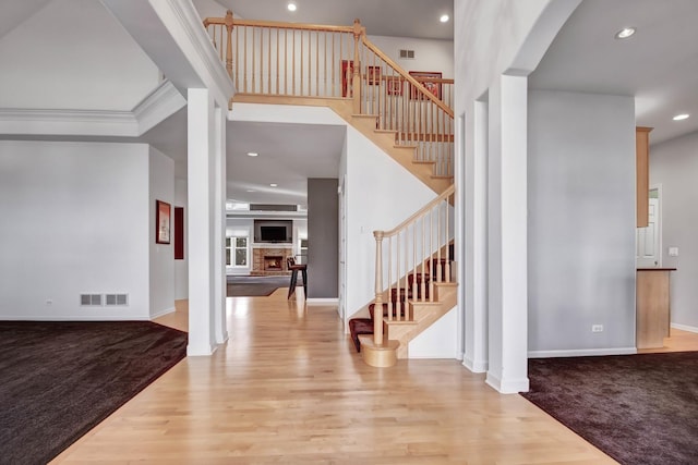 entryway with decorative columns, crown molding, a towering ceiling, a fireplace, and hardwood / wood-style floors