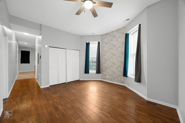 unfurnished bedroom featuring wood-type flooring, a closet, ceiling fan, and brick wall