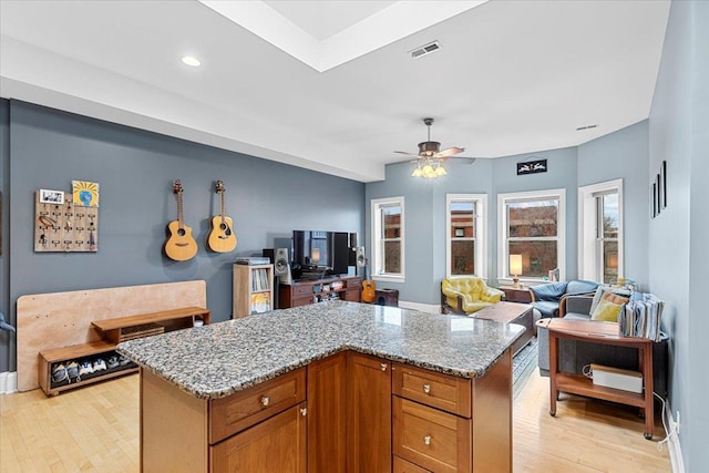 kitchen featuring light hardwood / wood-style flooring, light stone countertops, ceiling fan, and a kitchen island