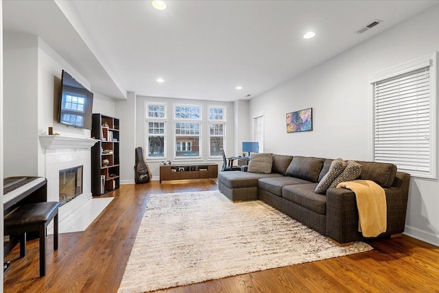 living area featuring a fireplace with flush hearth, visible vents, dark wood-style flooring, and recessed lighting