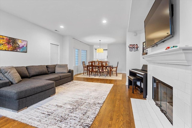 living room featuring a tile fireplace, recessed lighting, wood finished floors, visible vents, and baseboards