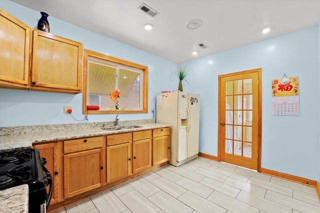 kitchen featuring white refrigerator with ice dispenser, sink, black range, and light stone counters