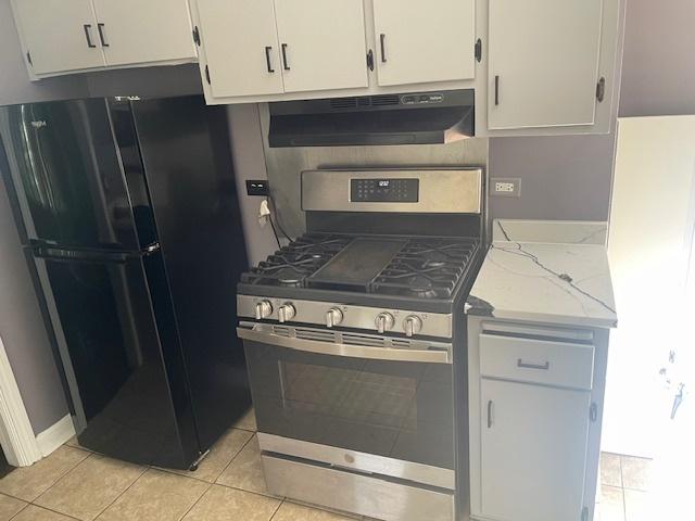 kitchen with light tile patterned floors, black refrigerator, white cabinetry, light stone countertops, and gas range