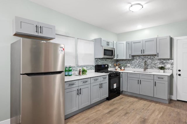 kitchen with tasteful backsplash, stainless steel appliances, sink, and light hardwood / wood-style flooring