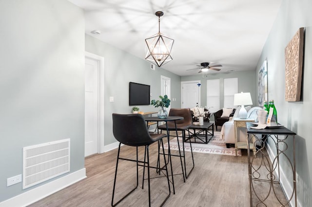 dining space with wood-type flooring and ceiling fan with notable chandelier