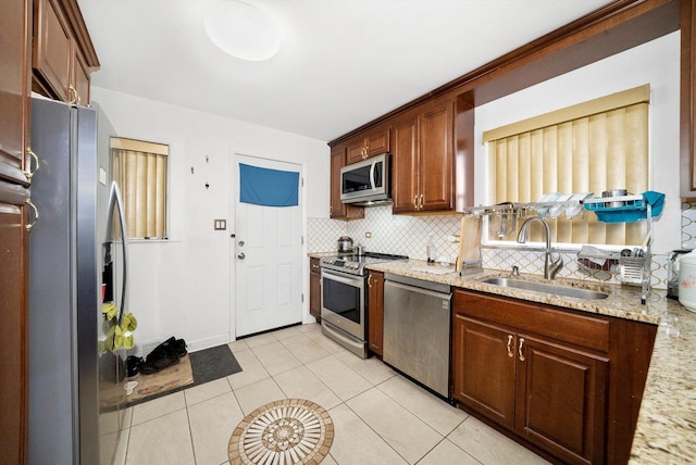 kitchen featuring sink, light tile patterned floors, stainless steel appliances, tasteful backsplash, and light stone counters