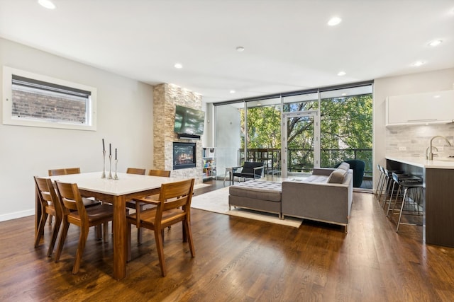 dining area featuring dark hardwood / wood-style floors, a wall of windows, a stone fireplace, and sink