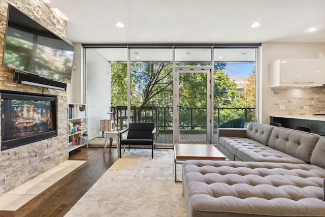 living room with floor to ceiling windows, a stone fireplace, and dark hardwood / wood-style flooring