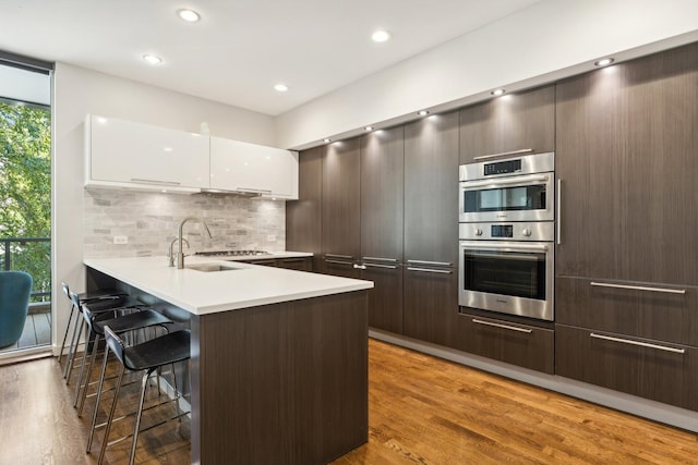 kitchen featuring white cabinets, a kitchen breakfast bar, decorative backsplash, kitchen peninsula, and stainless steel double oven