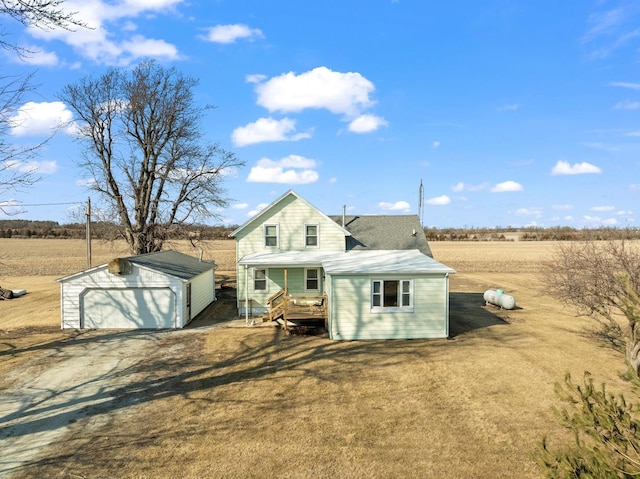 rear view of property featuring an outbuilding, a detached garage, dirt driveway, a lawn, and a rural view