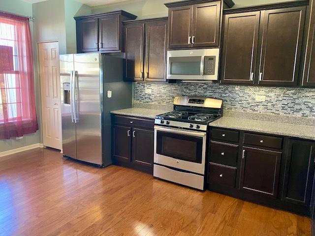 kitchen featuring backsplash, stainless steel appliances, dark brown cabinets, and light wood-type flooring