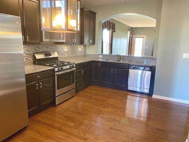 kitchen featuring appliances with stainless steel finishes, wood-type flooring, sink, decorative backsplash, and dark brown cabinetry