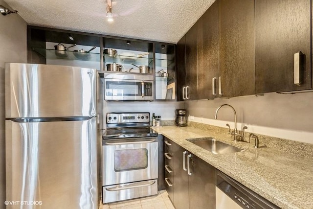 kitchen with sink, appliances with stainless steel finishes, light stone counters, dark brown cabinetry, and a textured ceiling