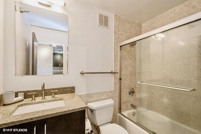 full bathroom with vanity, tile walls, shower / bath combination with glass door, and toilet