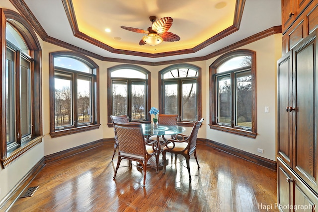 dining space featuring hardwood / wood-style floors, a tray ceiling, ornamental molding, and ceiling fan