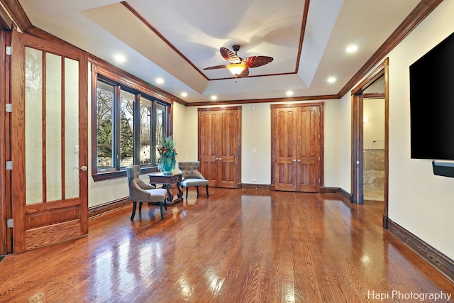 living area with hardwood / wood-style floors, crown molding, a raised ceiling, and ceiling fan