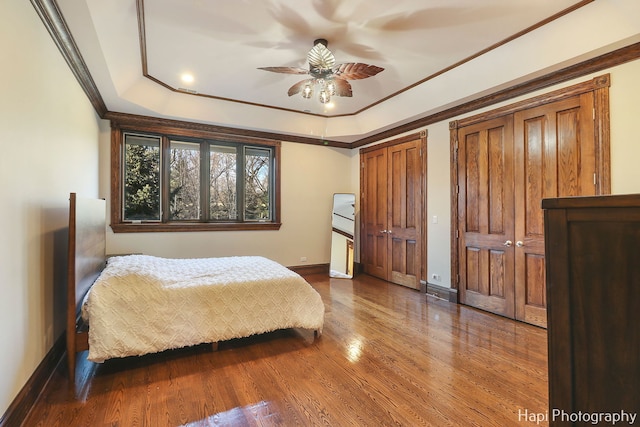 bedroom with two closets, hardwood / wood-style floors, ceiling fan, a tray ceiling, and crown molding