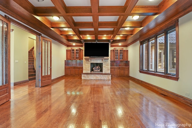 unfurnished living room featuring coffered ceiling, a stone fireplace, beam ceiling, and light hardwood / wood-style flooring