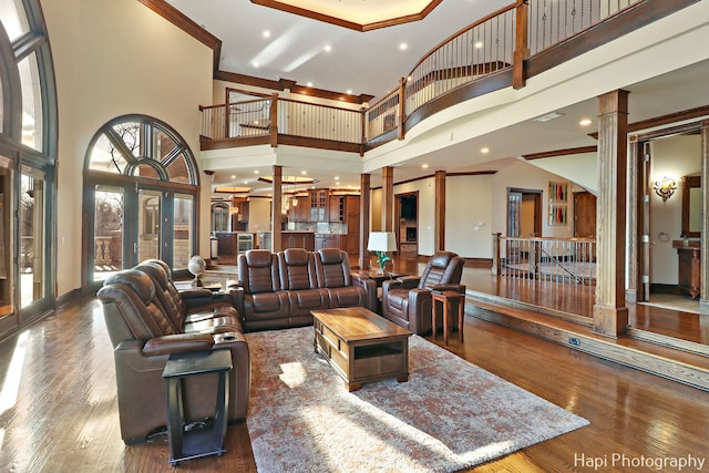 living room with crown molding, hardwood / wood-style flooring, decorative columns, and a high ceiling